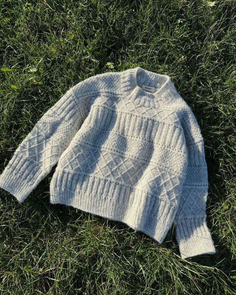 Lysegrå Ingrid Sweater liggende på græs