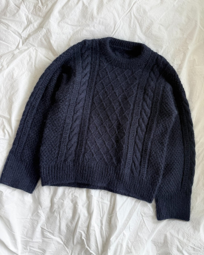 Blå Moby Sweater liggende på sengetøj