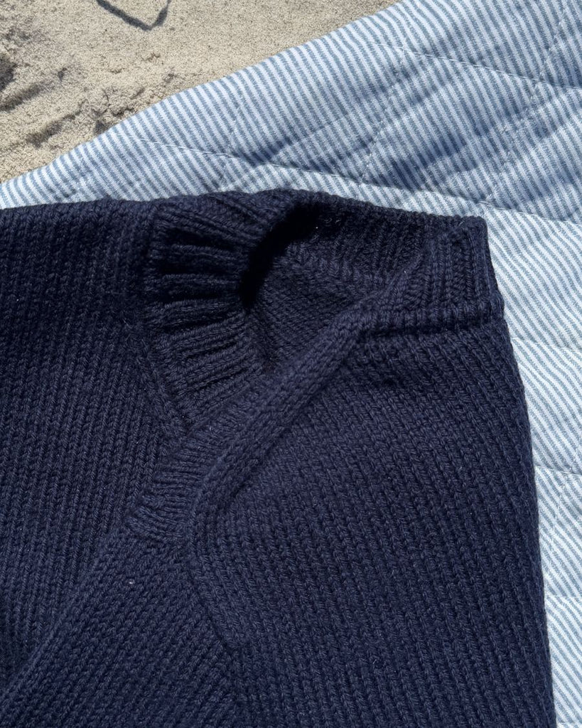 Blå Vega Sweater på strandtæppe med fokus på skulderen