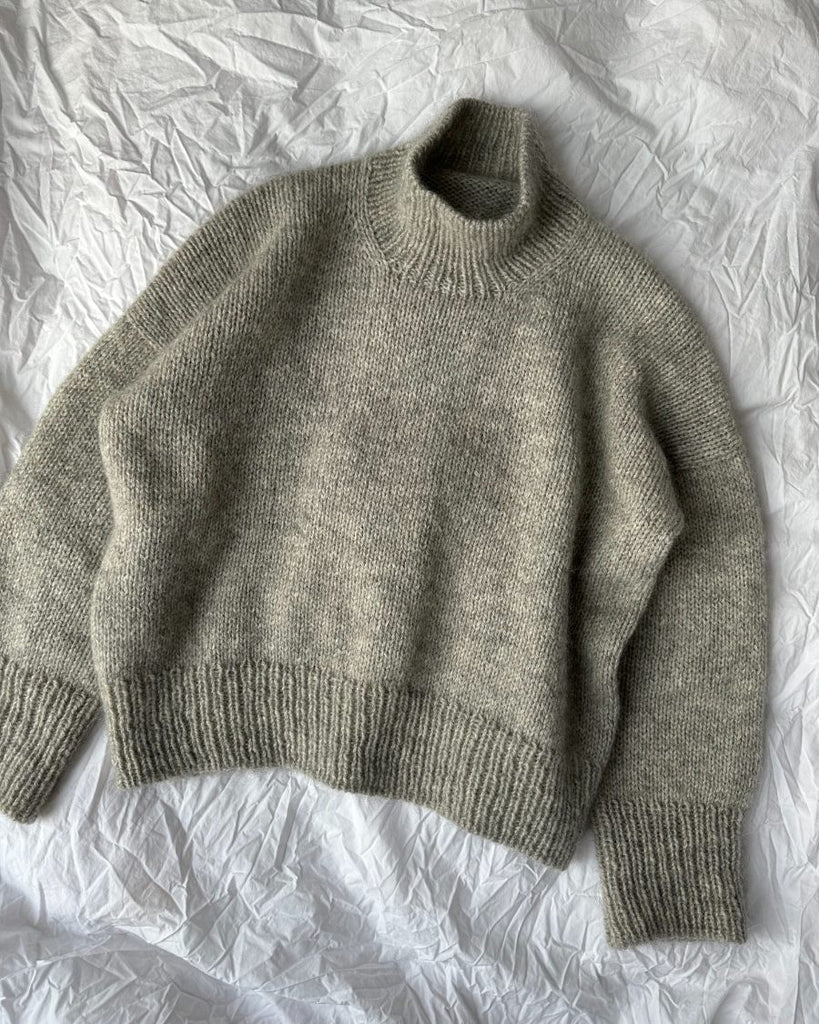 Lysegrå Weekend Sweater liggende på dyne