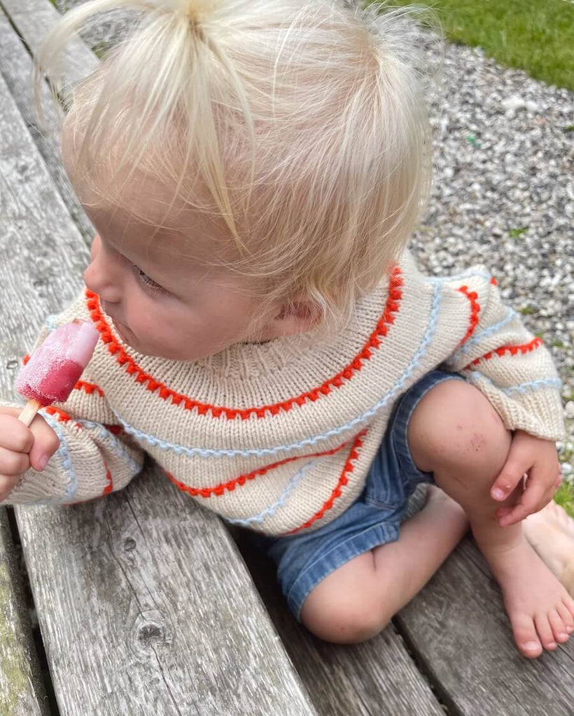 Barn iført Festival Sweater med hvide, blå og orange striber
